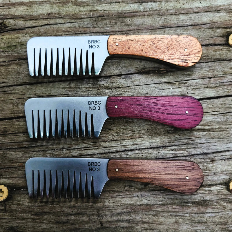 Big Red No. 3 stainless steel beard combs with mahogany, purpleheart, and walnut handles on a wood bench