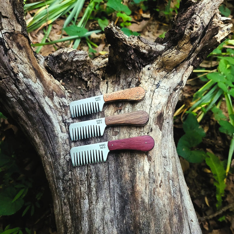 Three Big Red No. 3 stainless steel beard combs with mahogany, walnut and purpleheart handles on a rustic log