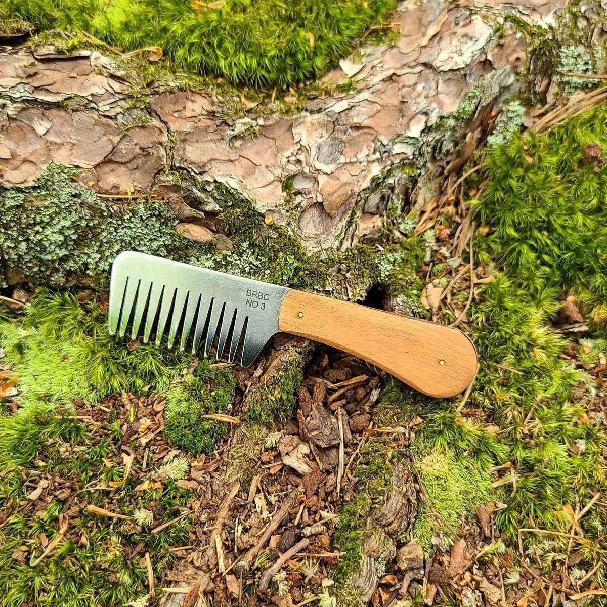 No. 3 stainless steel beard comb with a natural cherry wood handle displayed on mossy tree root