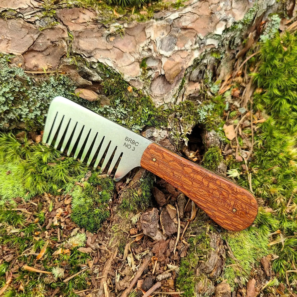 No. 3 stainless steel beard comb with a natural leopardwood handle displayed on mossy tree root