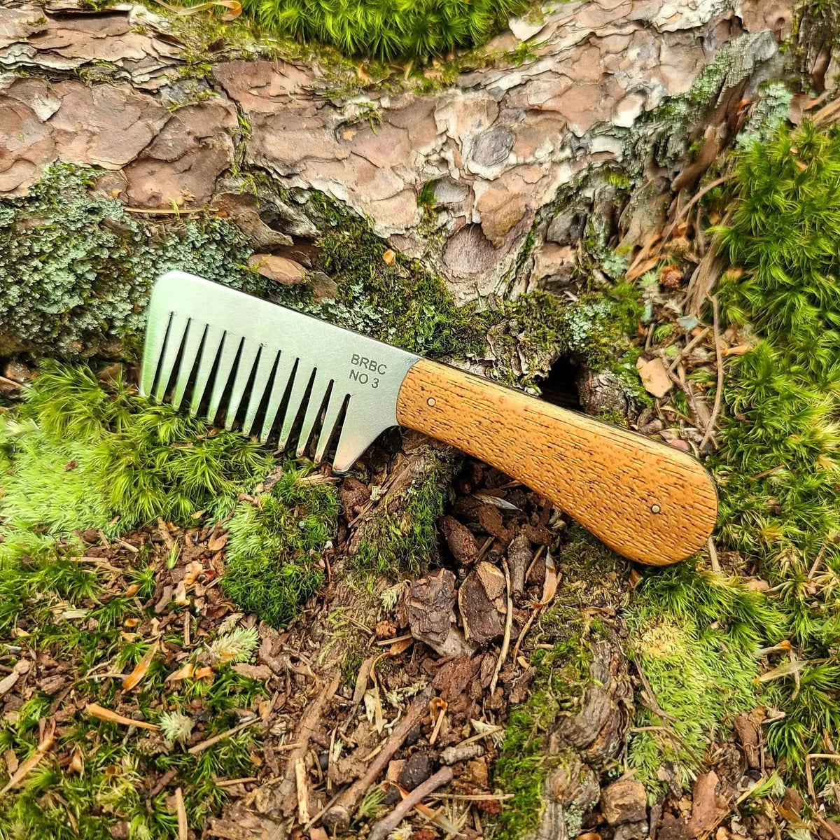 No. 3 stainless steel beard comb with a natural mahogany wood handle displayed on mossy tree root