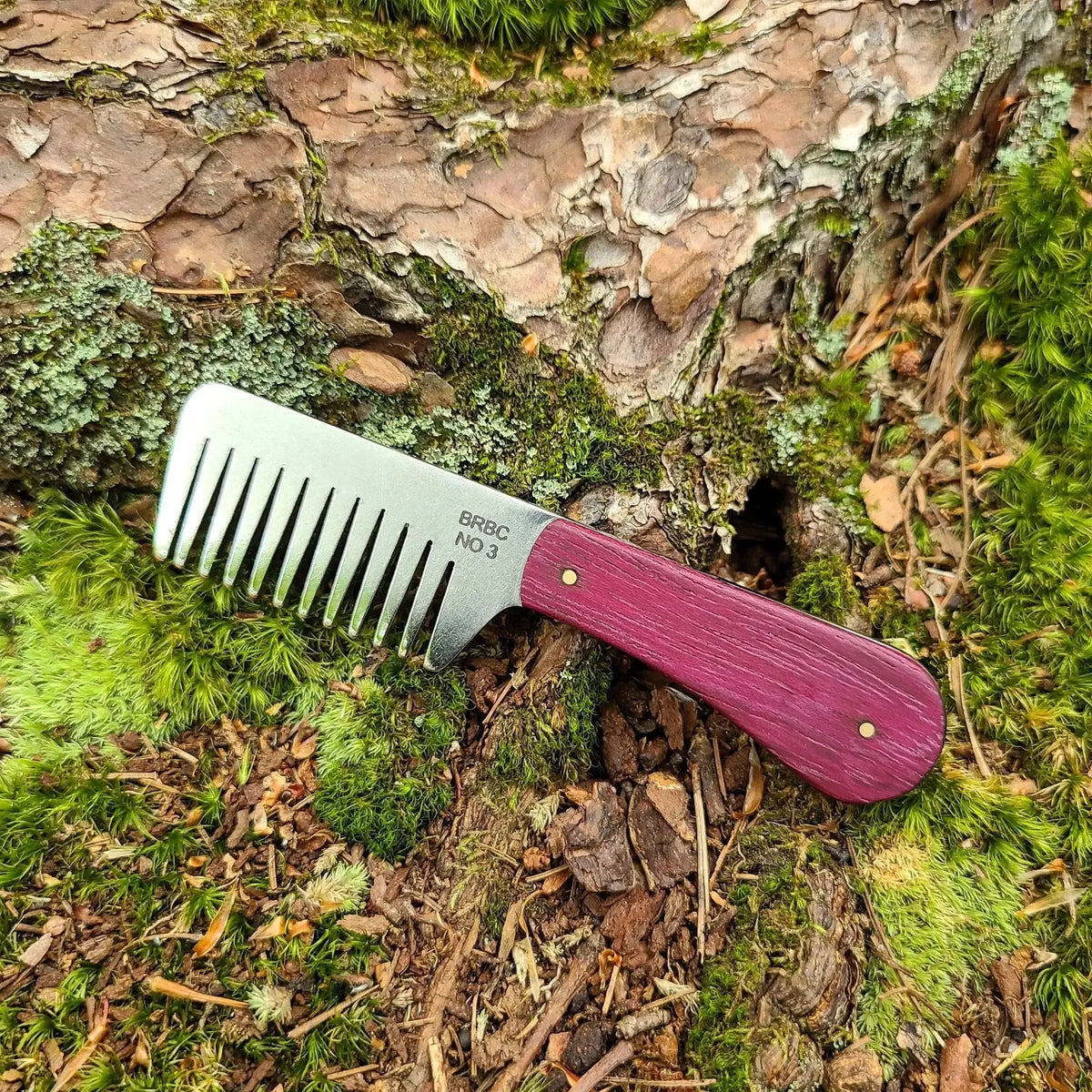 No. 3 stainless steel beard comb with a natural purpleheart wood handle displayed on mossy tree root