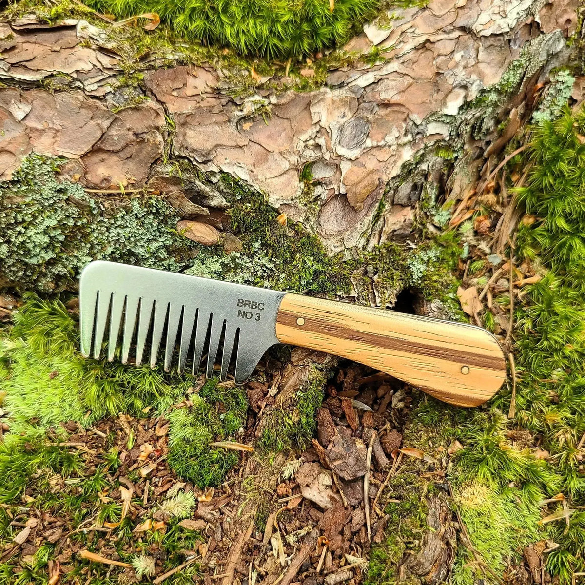 No. 3 stainless steel beard comb with a natural zebrawood handle displayed on mossy tree root