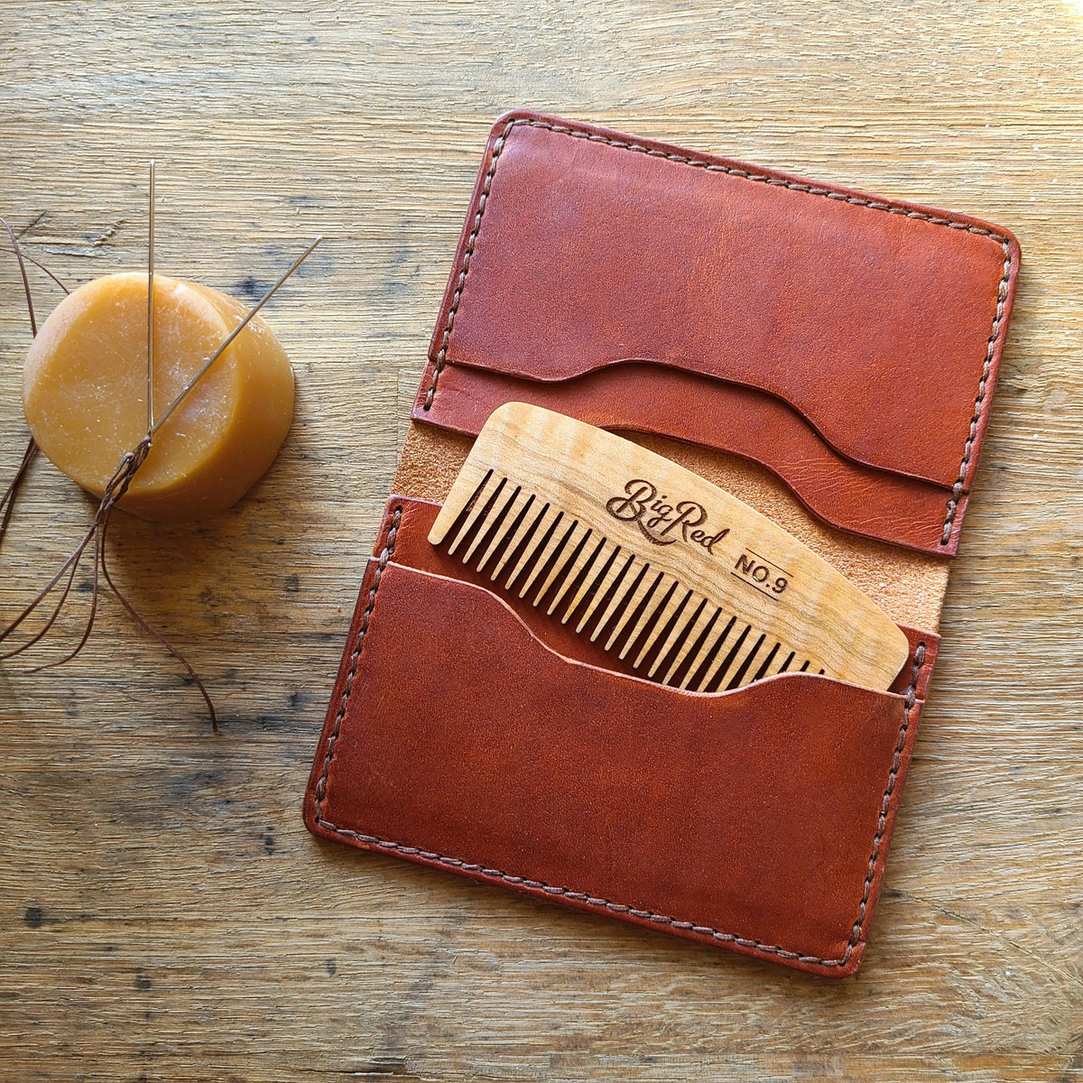 Brown leather wallet with wooden comb on a wooden surface